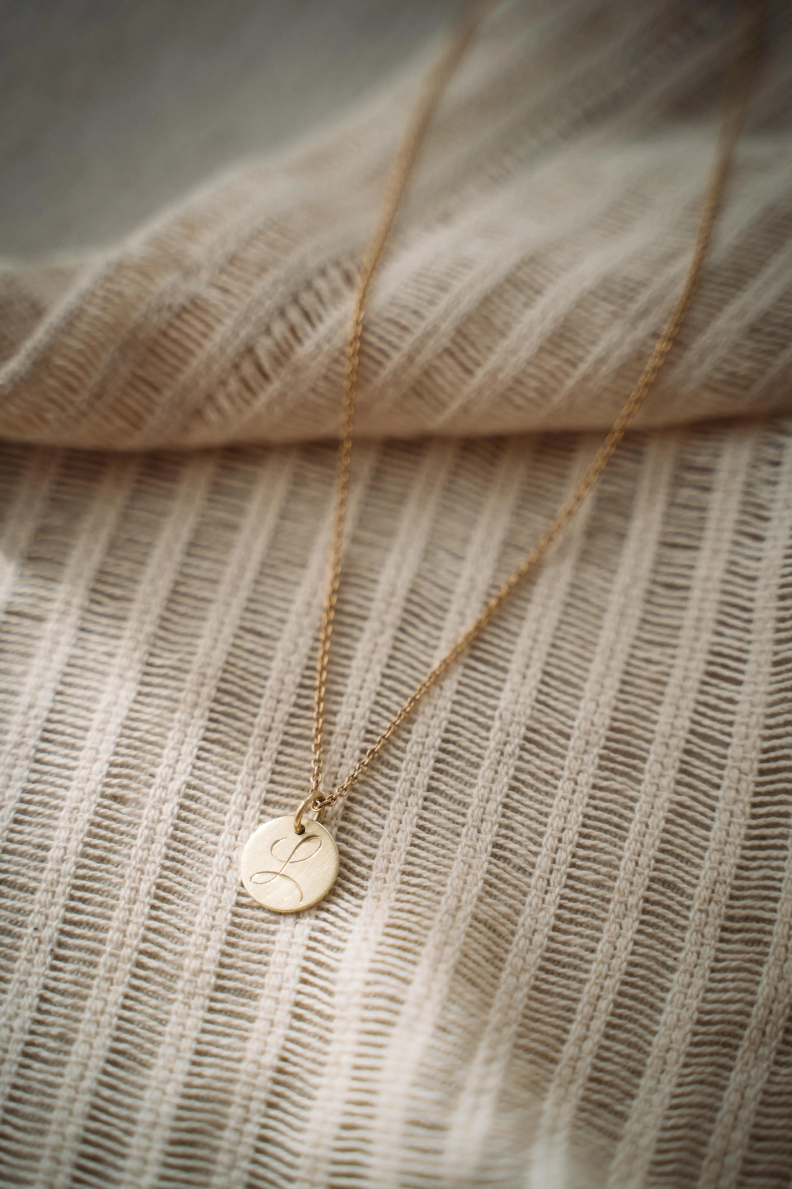 Goldkette mit rundem Anhänger und graviertem Initial L auf Leinenstoff