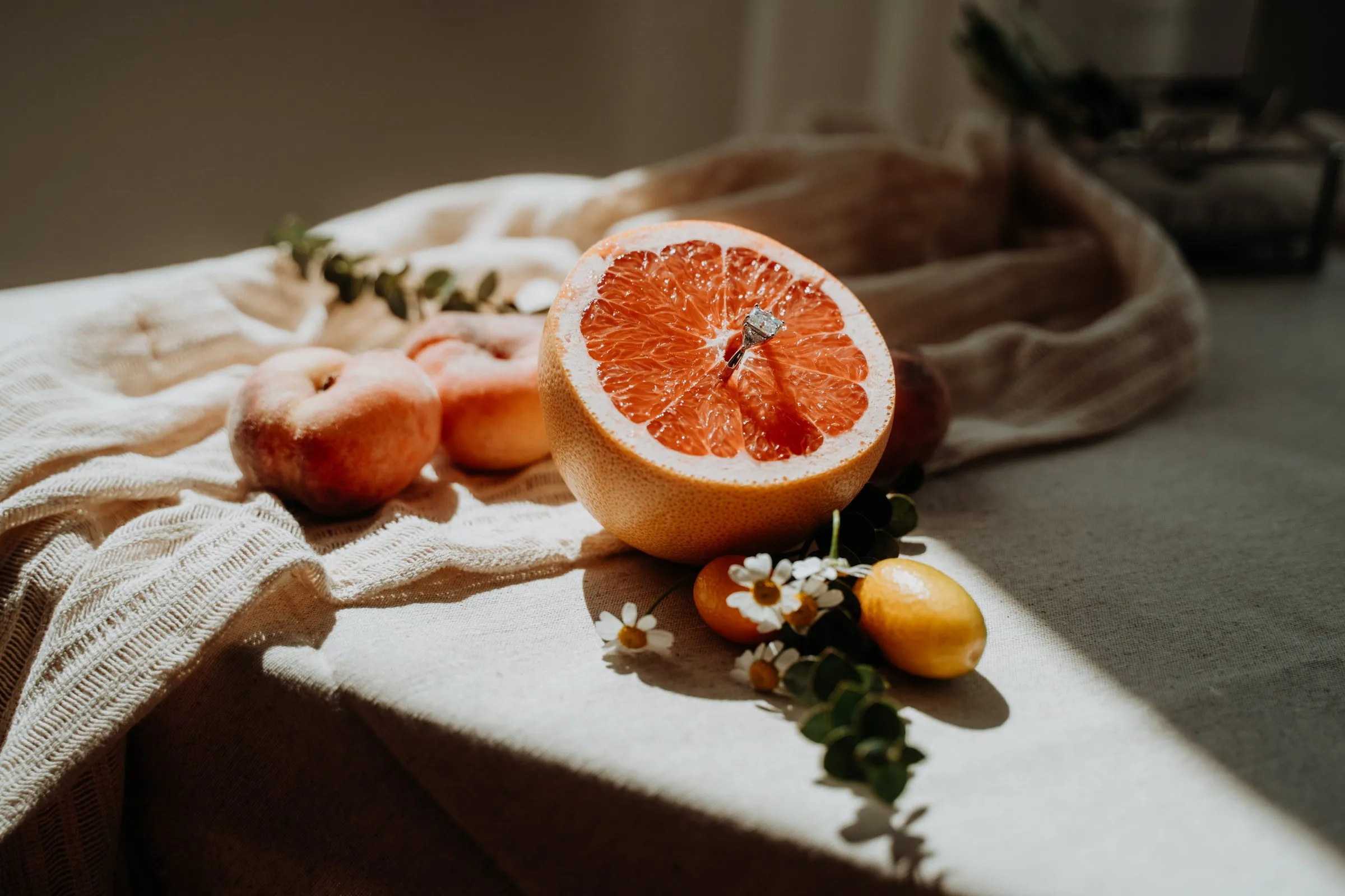 Stillleben mit Grapefruit, Pfirsichen und handgefertigten Ringen im Sonnenlicht