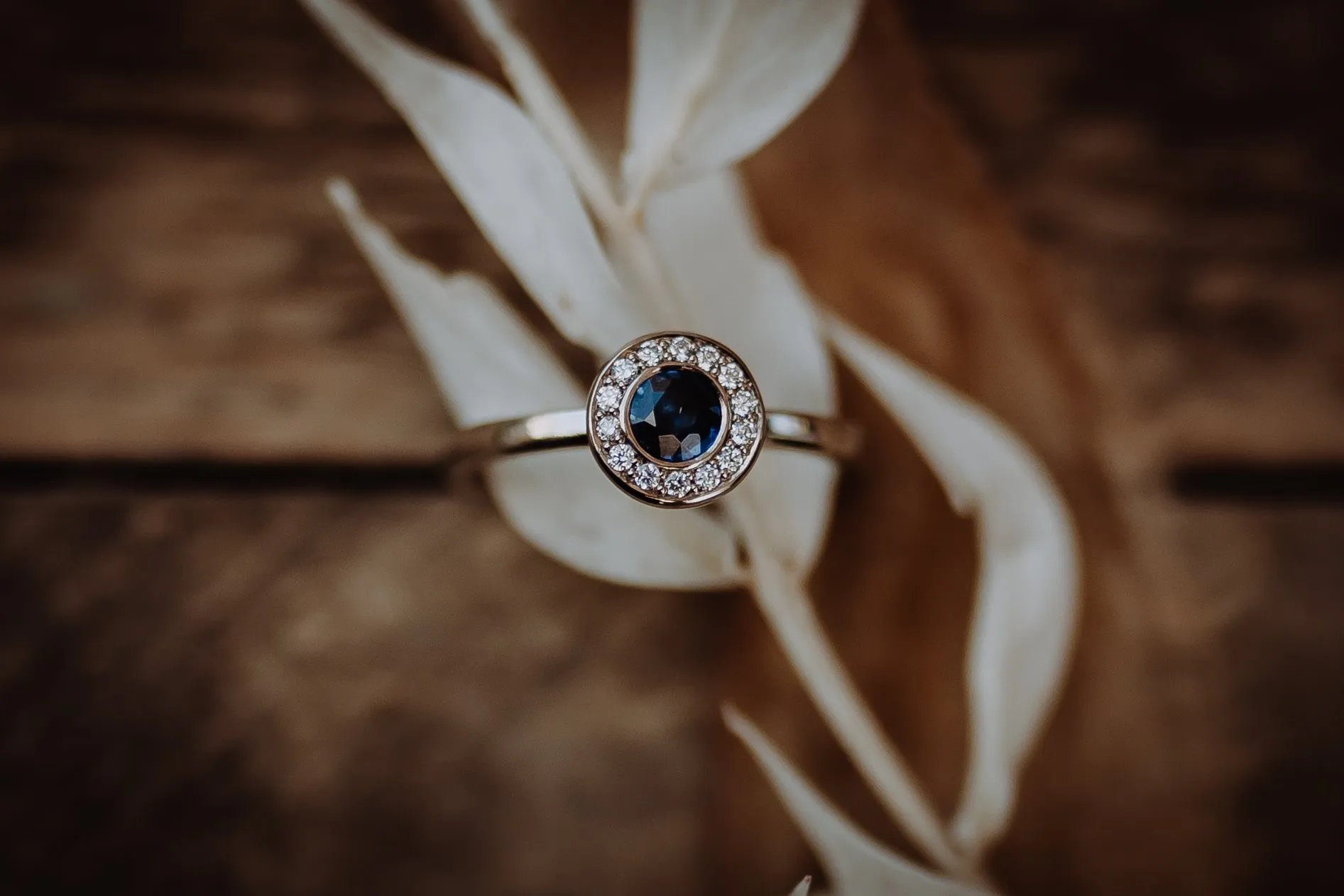 Verlobungsring mit blauem Saphir im Diamantkranz auf hellen Zweigen